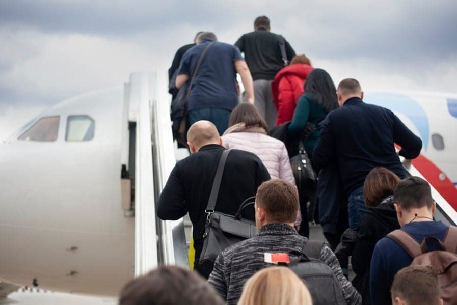 Passengers carrying bags and backpacks climbing a boarding staircase onto a commercial airliner under an overcast sky
