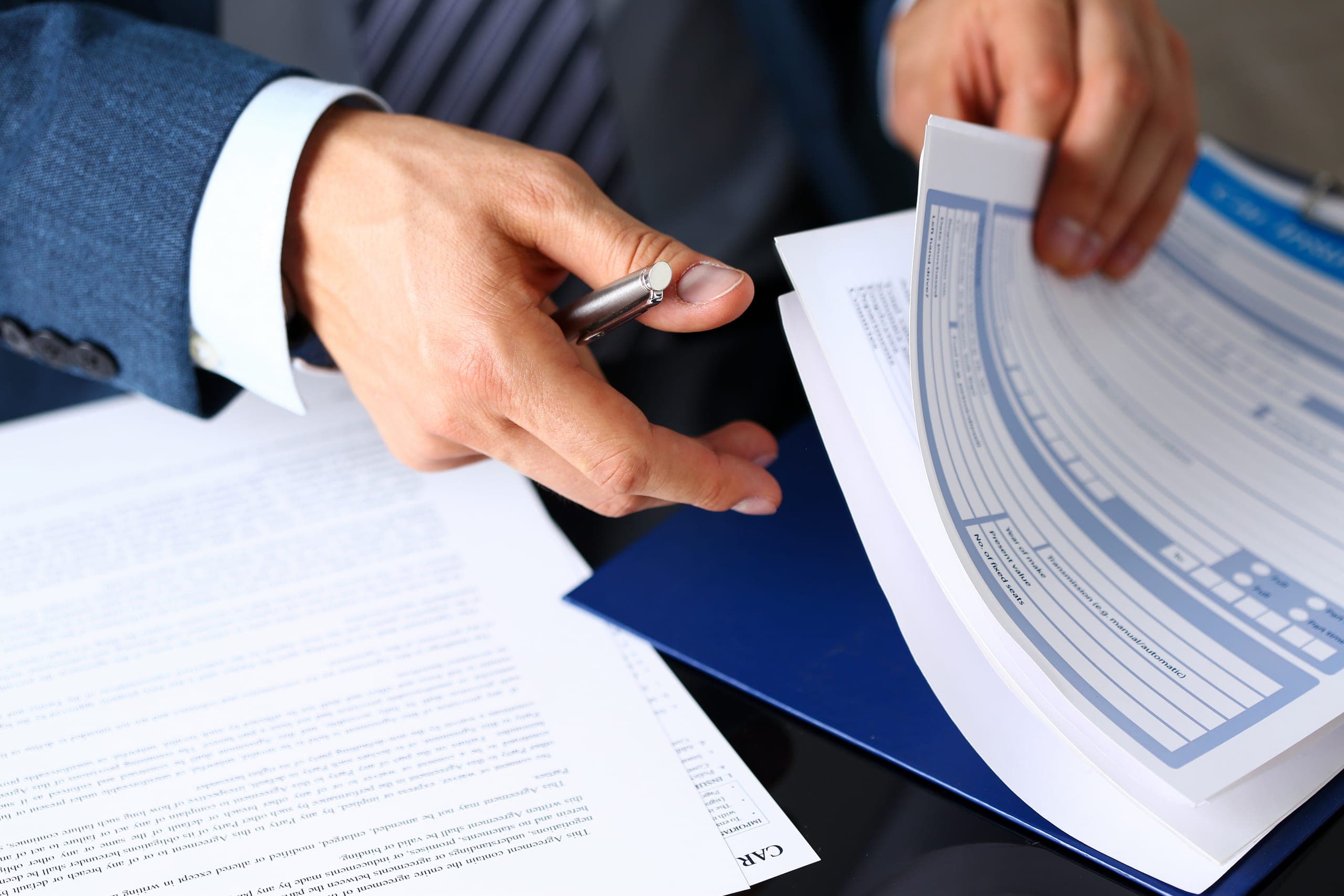 Close-up of hands reviewing insurance documents and a clipboard with a pen at a desk