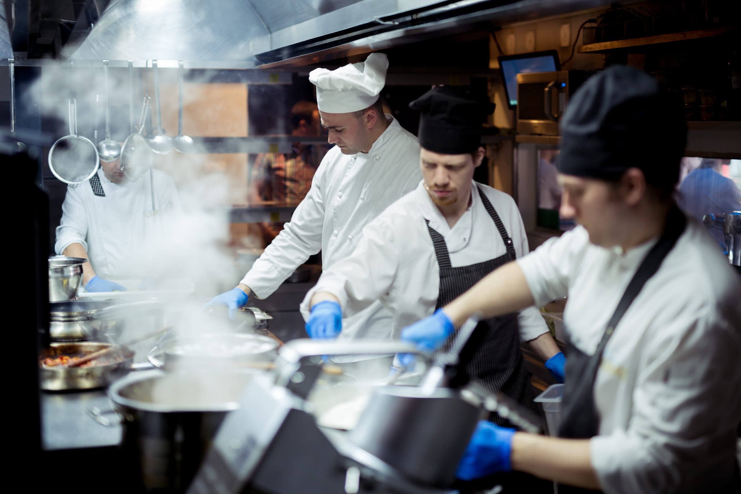 Chefs in white uniforms and hats preparing food in a busy commercial kitchen
